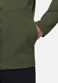 Giacca verde a conchiglia morbida con zip frontale, colletto alto e silhouette aderente, caratterizzata da una texture liscia e senza motivi visibili.