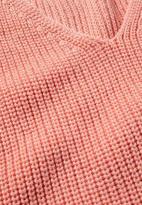 Gestrickter Pullover in Hellpink mit V-Ausschnitt, der ein strukturiertes Muster und eine lockere Passform aufweist. Der Stoff ist weich und hat sichtbare Nähte.