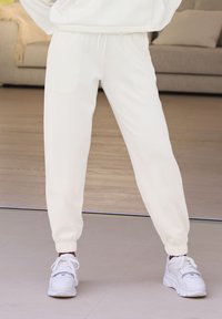 Biele joggingové nohavice vyrobené z mäkkej, elastickej látky s elastickými manžetami a vreckami. Spárované s bielymi teniskami pre ležérny vzhľad.
