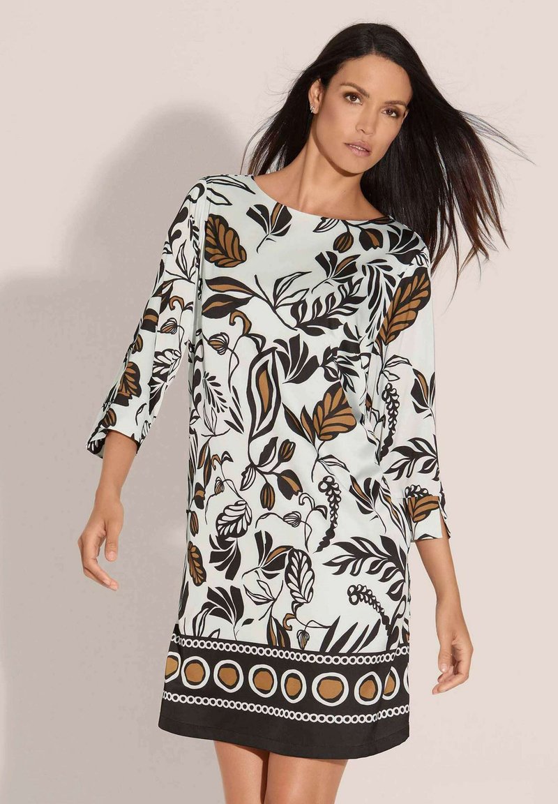 Hellblaues Kleid mit schwarz-braunem botanischem Druck, Dreiviertelärmel und einem Saum, der durch kreisförmige und geometrische Muster akzentuiert ist.