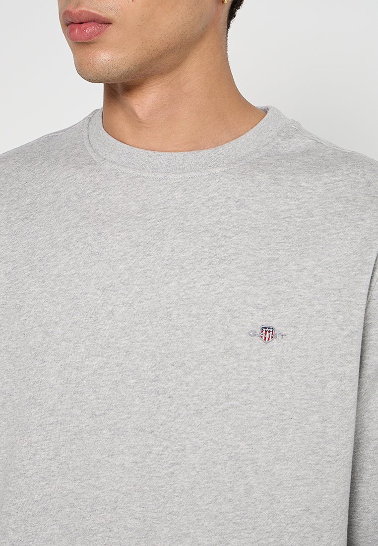 Szary sweatshirt wykonany z teksturowanej bawełny, z okrągłym dekoltem i małym haftowanym logo na piersi. Prosty, codzienny design.