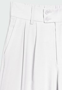 Pantalon en tissu blanc tissé avec des plis à l'avant. Il présente une ceinture plate avec deux boutons assortis et des poches latérales.