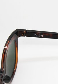 Kilpikonnakuosisilmälasit tummilla harmailla laseilla, rohkeassa suorakulmaisessa muodossa, ja mustissa varsissa, joissa lukee hopeanvärisellä "Palm".