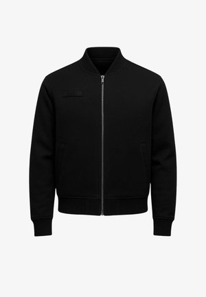 Giacca nera con zip in tessuto strutturato, colletto alto, due tasche laterali e etichetta con logo sul petto.