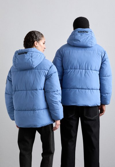 Hellblaue Pufferjacken mit Kapuze, die ein gestepptes Design und ein Logo auf dem Rücken aufweisen, kombiniert mit schwarzen Hosen, von hinten betrachtet.