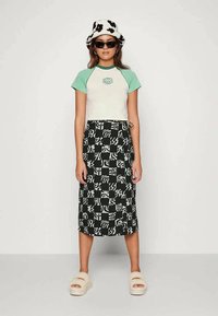 T-shirt com mangas verde menta e corpo branco, combinado com uma saia midi preta e branca com padrão e sandálias felpudas. Chapéu de balde com padrão de vaca.