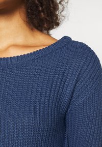 Pull bleu côtelé avec un large décolleté et un motif tricoté texturé, présentant une vue en gros plan du tissu et des détails de couture.