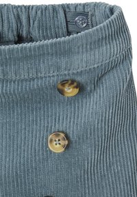 Blaues Cordstoffgewebe mit vertikalen Rippen, das zwei braun marmorierte Knöpfe und einen verstellbaren elastischen Bund mit einem blauen Knopf aufweist.