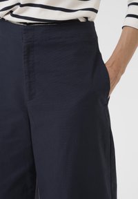 Navy blue wide-leg pants made of lightweight cotton blend, featuring side pockets and a smooth texture. Visible stitching along seams.