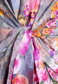 Tissu à motif floral présentant des nuances de rose, d'orange et de violet, avec une texture douce et légère, rassemblé et noué au centre.