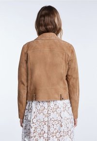 Chaqueta de ante color canela con diseño ajustado, cuello con muesca y costuras visibles. La parte trasera presenta dos aberturas laterales con herrajes negros.