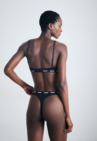 Black lingerie set featuring adjustable straps, logo band, and thong design. Smooth fabric with minimal coverage, emphasizing contoured fit.
