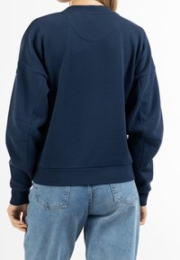 Sweat-shirt bleu marine à encolure arrondie, coupe ample et tissu texturé. Présente des poignets et un ourlet côtelés, porté par un modèle vu de dos.