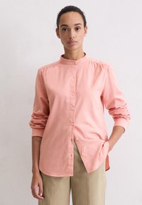 Light pink shirt with a stand-up collar, long sleeves, and button closure. Made from smooth fabric with minimal detailing.