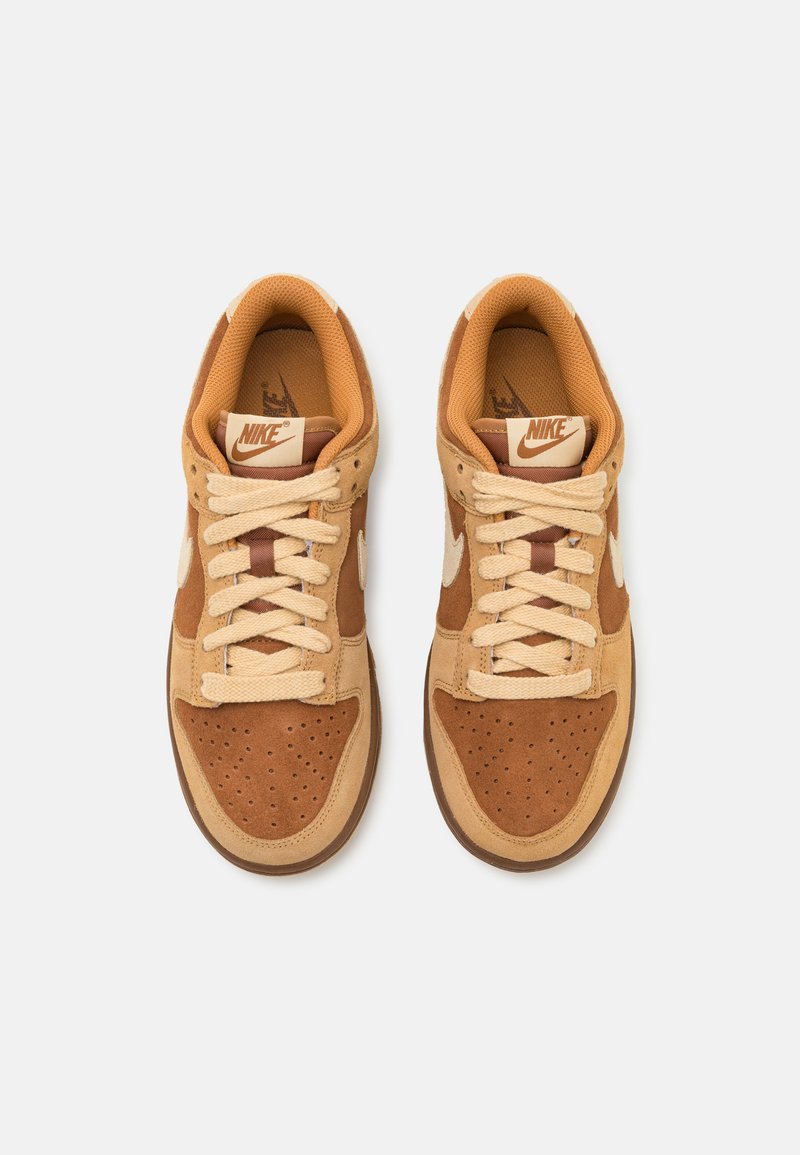 Nike sneakers hebben een tan suède bovenwerk, beige leren accenten, ronde veters en perforaties op de neus voor ademend vermogen.