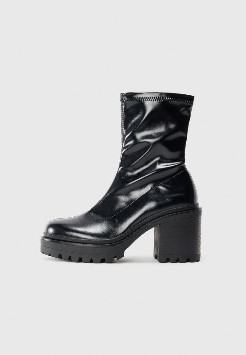 Botte en cuir noire mi-mollet avec un large talon bloc et une semelle à rainures, présentée de profil sur un fond clair.