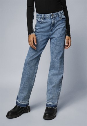 Lyseblå denimjeans med rette ben, falmet tekstur og frynset søm. Kombinert med svarte klumpete sko og en langermet svart topp.