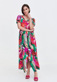 Maxi sukienka wykonana z lekkiego materiału z żywym kwiatowym wzorem w kolorze różowym, zielonym i pomarańczowym, z krótkimi bufkami i rozcięciem z przodu.