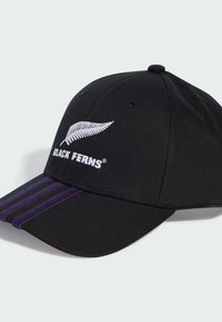 Gorra de béisbol negra con logo blanco de helecho y texto "BLACK FERNS", que presenta tres rayas moradas en el lado izquierdo delantero del visera.