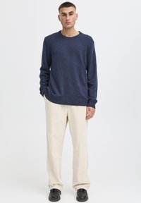 Granatowy sweter z dzianiny z okrągłym dekoltem, w zestawieniu z kremowymi sztruksowymi spodniami i czarnymi butami. Strój charakteryzuje się luźnym krojem.