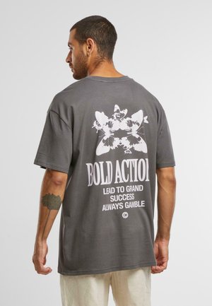 Grå kortærmet t-shirt med et stort hvidt grafisk print på ryggen med tekst og sommerfuglemotiver. Løs pasform, lavet af bomuld.