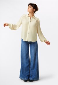 Camicia button-up beige chiaro con maniche a palloncino, abbinata a jeans blu a vita alta e gamba larga in una classica trama di denim.