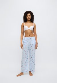 Pantalon de pyjama bleu clair à pois rouges et rayures verticales, associé à un soutien-gorge blanc. Coupe ample, tissu léger, conçu pour le confort.