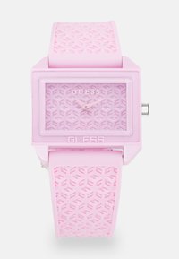 Montre en silicone rose avec un cadran carré, bracelet texturé présentant un motif géométrique, et un cadran minimaliste avec des aiguilles et un logo argentés.