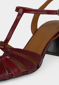 Ανοιχτή σανδάλι από δέρμα μπορντό με πολλαπλούς μπροστινούς ιμάντες, σχέδιο T-ιμάντα, ταμπά πάτο και χαμηλό μαύρο τακούνι μπλοκ.