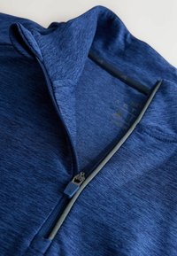 Blaues sportliches Zip-Up-Oberteil aus strukturiertem Stoff, mit hohem Kragen und grauem Reißverschluss. Gehört ein Logo in der Nähe des Reißverschlusses und hat ein elegantes Design.