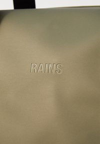 Khaki zöld vízálló táska, amelyen a "RAINS" logó dombornyomott. Sima textúrájú, téglalap alakú és minimalista dizájnnal rendelkezik. Állítható pántot tartalmaz.