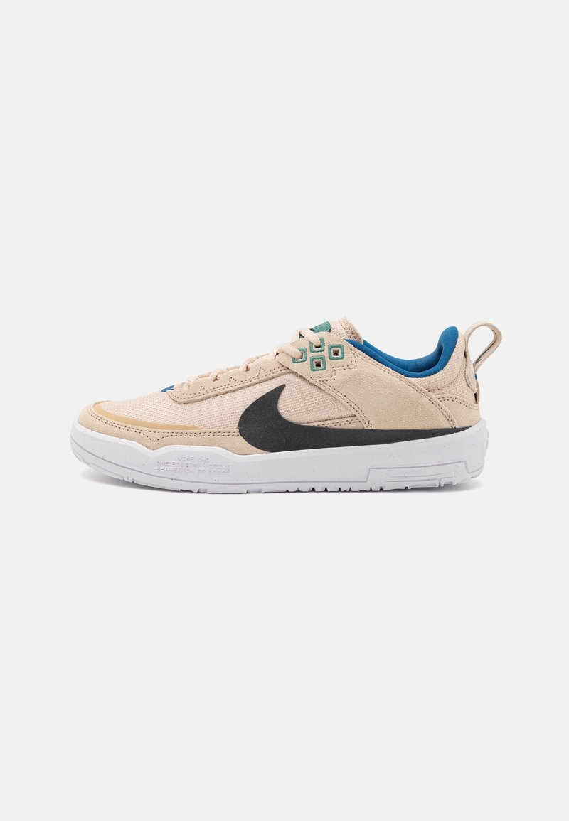 Baskets basses beiges avec un swoosh noir, une semelle blanche, une doublure intérieure bleue, des œillets verts et une languette au talon.