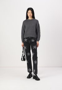 Grå strikket genser, svarte jeans med sølvstjernemønster, svart håndveske og svarte kraftige sko. Glatt tekstur og avslappet passform.