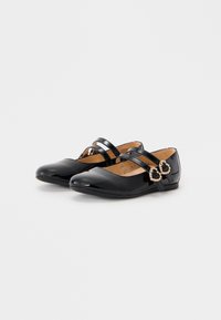 Svarte lakkflats med rund tå, med to kryssende stropper og en dekorativ spenne på siden. Glatt tekstur og minimalistisk design.