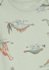 Zelena tkanina s ilustracijama raznih dinosaura, uključujući stegosaura, brahiosaura i vrste s bodljikavim repom, u prigušenim plavim i narančastim tonovima.
