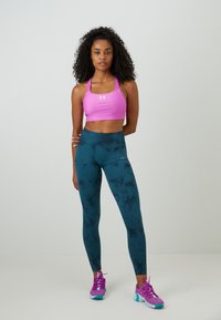 Rosa Sport-BH mit einem Logo, türkisfarbene Leggings mit einem dunklen Marmor-Muster und lila Sportschuhe mit türkisfarbenen Akzenten.