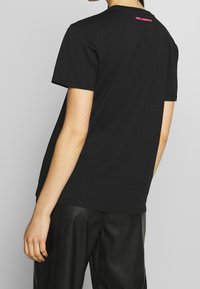 Czarny bawełniany t-shirt o luźnym kroju, z krótkimi rękawami i okrągłym dekoltem. Z tyłu znajduje się mały czerwony detal z logo przy kołnierzu.