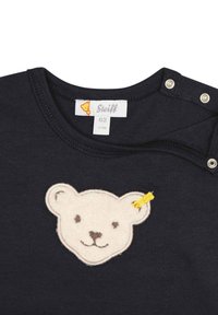 Camicia blu navy a maniche corte con un'applicazione in lana a forma di orso sulla parte anteriore. Dotata di chiusure a scatto sulla spalla. Etichetta visibile.