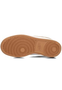 Suela de zapato con un exterior de goma marrón, patrones de relieve circulares, y una entresuela de color claro que presenta un logo visible y una textura moteada.