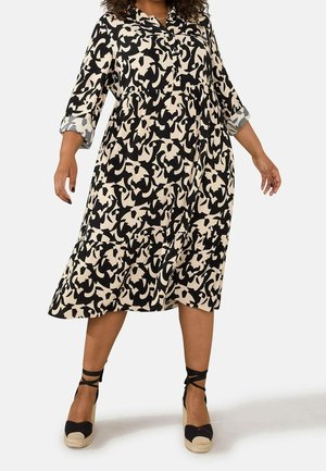 Femme portant une robe ample, longueur genou, à motif abstrait noir et blanc, manches 3/4 et sandales compensées espadrilles noires.