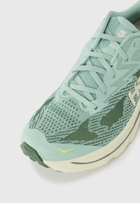 Laufschuh aus hellgrünem Mesh mit dunkleren grünen Akzenten. Verfügt über ein strukturiertes Obermaterial, einen gepolsterten Kragen und gelbe Details an der Zehenpartie.