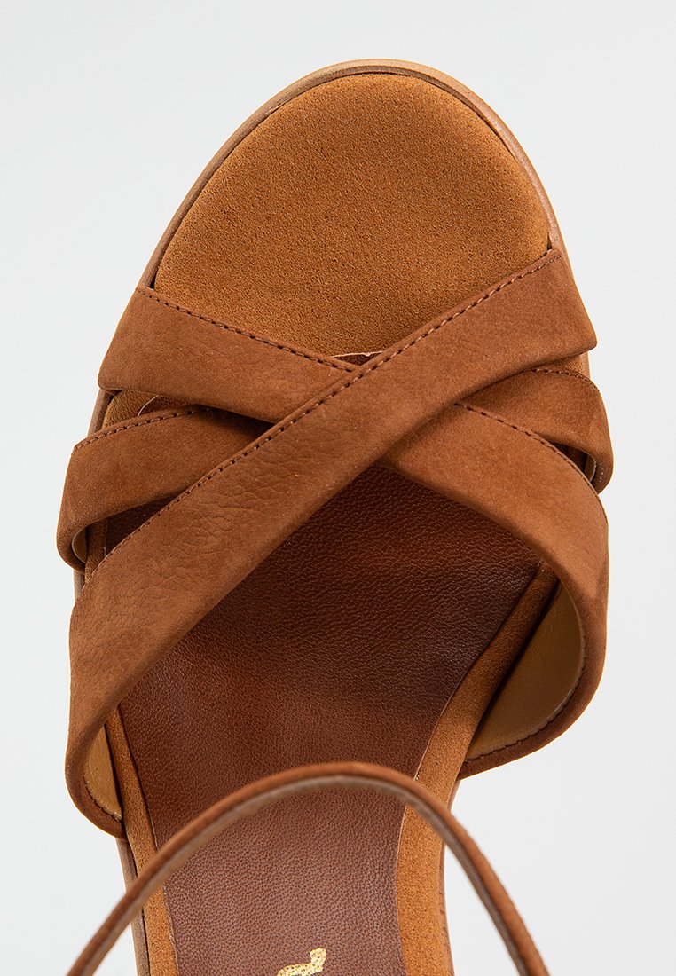 Sandalies à talons hauts en daim marron avec des brides croisées et un bout arrondi. Texture douce avec une doublure intérieure lisse et une semelle de plateforme.