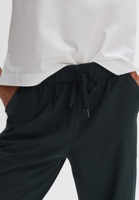 Schwarze Joggerhosen mit elastischem Bündchen und Kordelzug. Glattes, leichtes Material mit seitlichen Taschen und lässiger Passform.