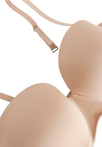 Soutien-gorge beige moulé avec bretelles ajustables, texture lisse, design classique et un éclat subtil sur le tissu, doté de soutien-armature.