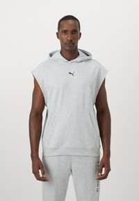 Siv na brezrokavnik s sprednjim žepom, narejen iz mehkih materialov. Ima črn Puma logo na prsih. Preprost, vsakdanji dizajn.