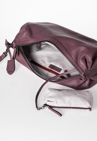 Paarse leren handtas met open rits die een patrooninterieur toont en een aparte bijpassende kleine ritszak op een witte achtergrond.