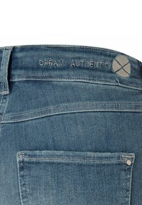 Gros plan sur la poche arrière d'un jean en denim bleu avec le nom de marque brodé "Dream Authentic" et un logo circulaire brodé sur la ceinture.