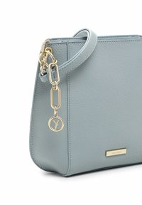Borsa a tracolla in pelle blu chiaro con finitura texturizzata, catena dorata attaccata e charm con logo. Forma rettangolare con chiusura a zip.