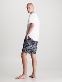 T-shirt bianca a maniche corte abbinata a pantaloni da bagno a righe nere e bianche, con un design astratto e una vestibilità comoda.