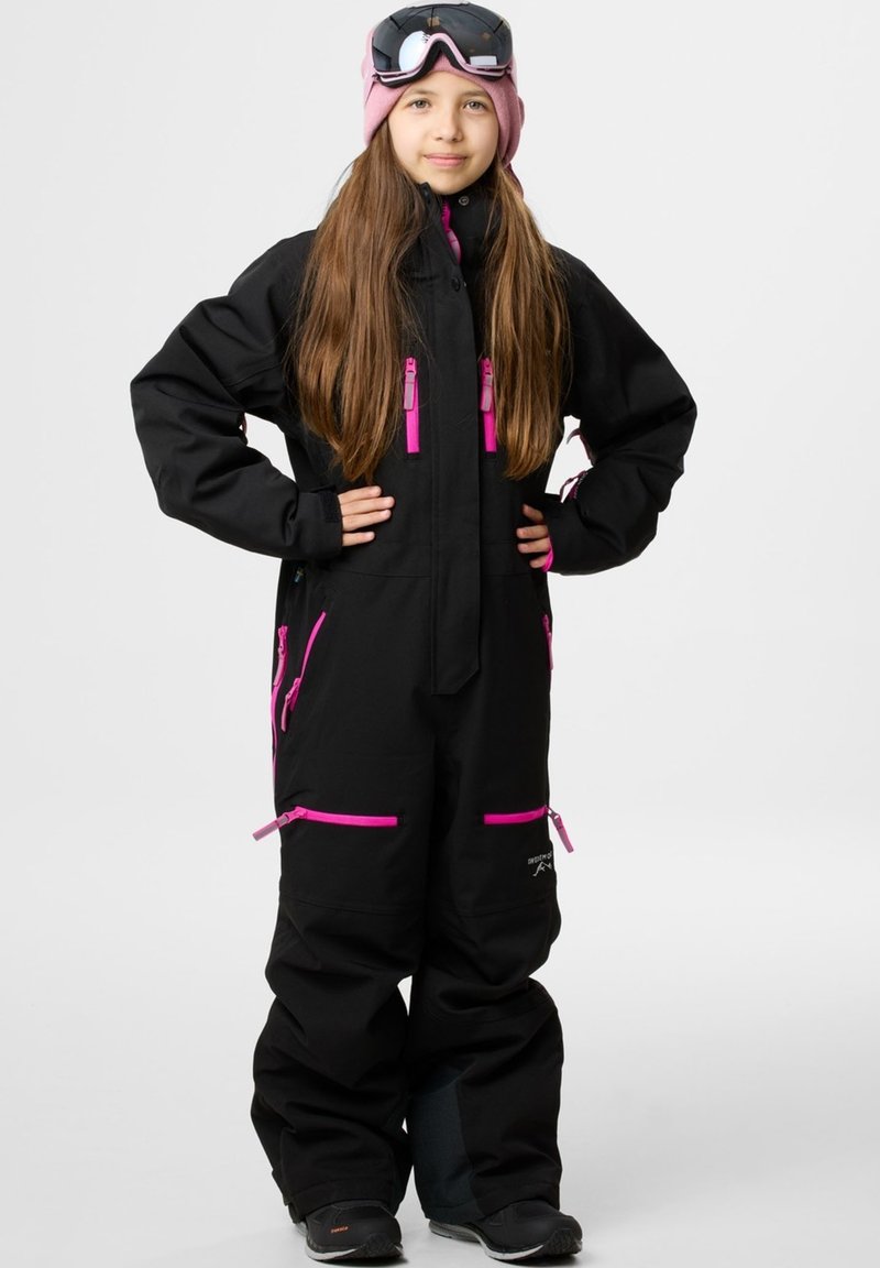 Zwarte skikleding met roze ritsen en accenten, voorzien van een hoge kraag, meerdere zakken en een losse pasvorm. Draagt een roze muts en een goggle.